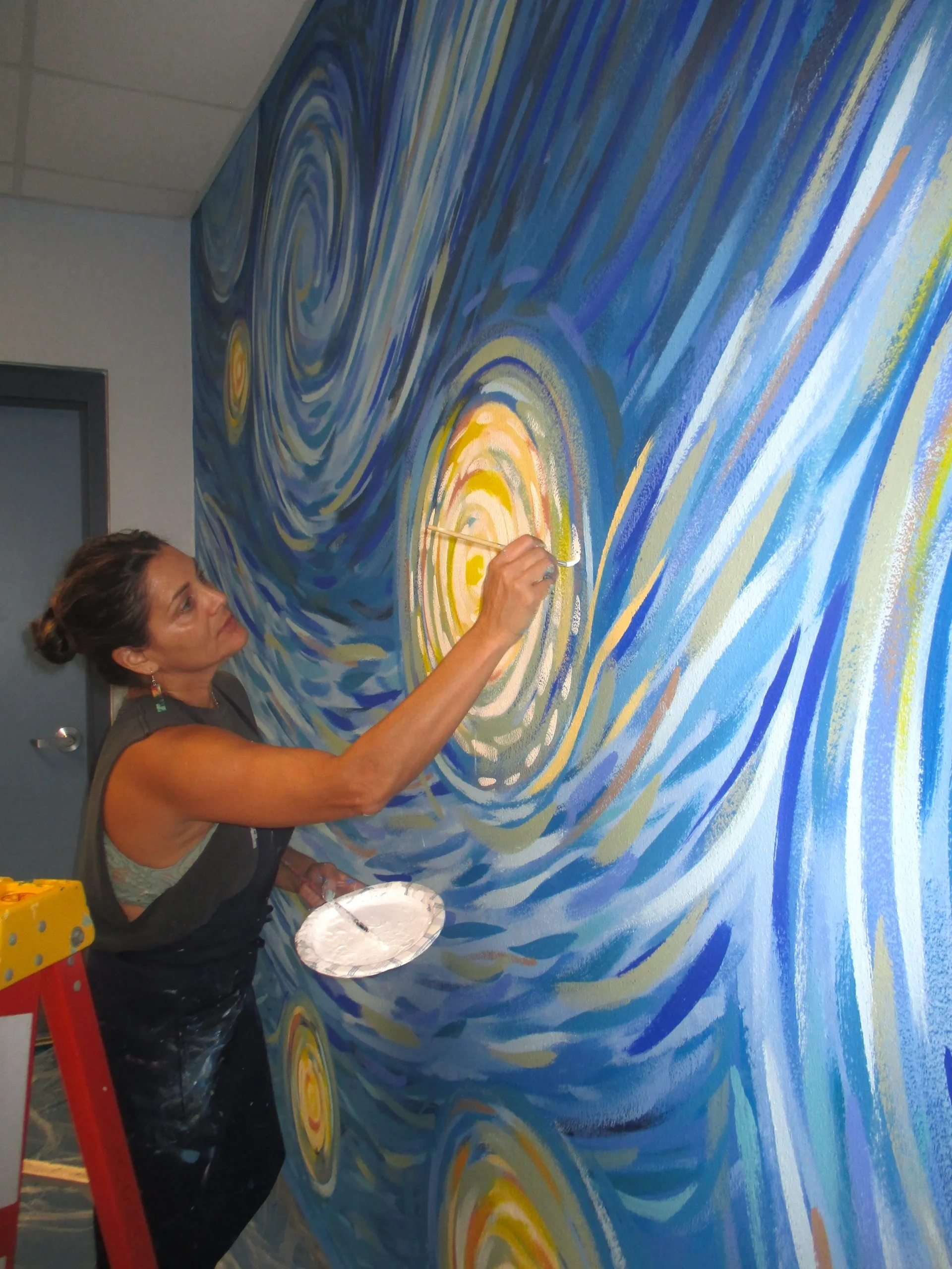 A woman painting a vibrant swirling mural on a wall.